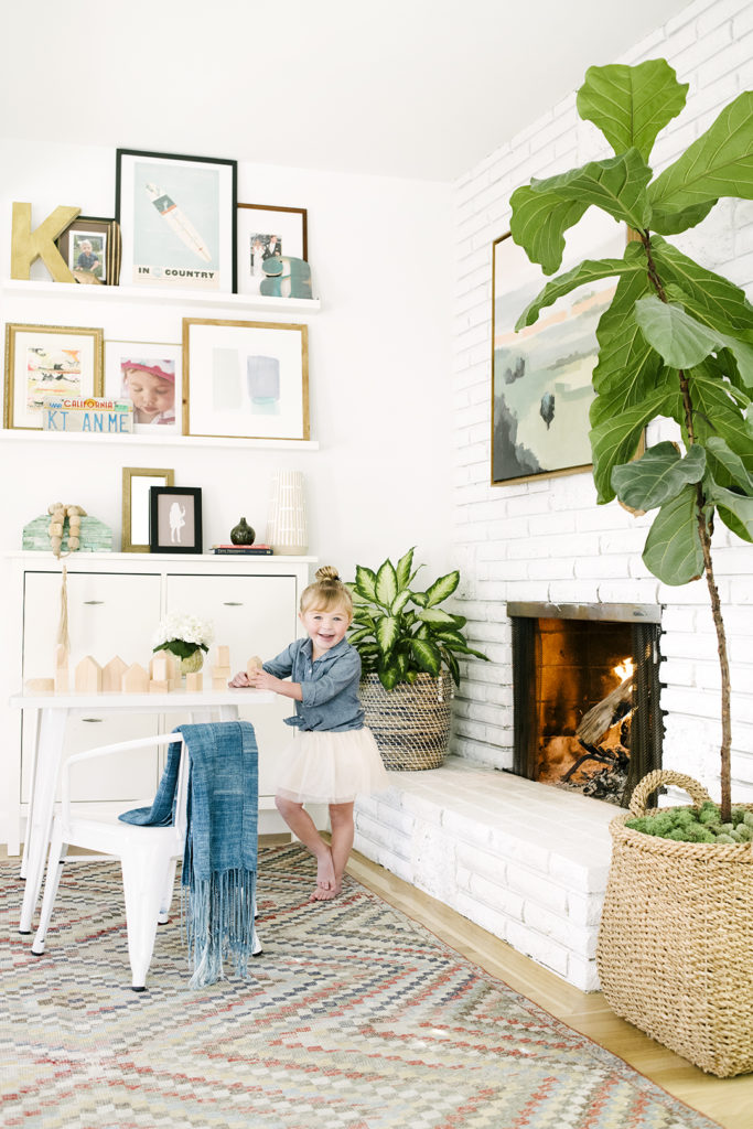 Family room with fireplace white brick fireplace and built in cabinet and floating shelves vintage Turkish rug fig leaf tree and kids play table designed by Kate Lester Interiors